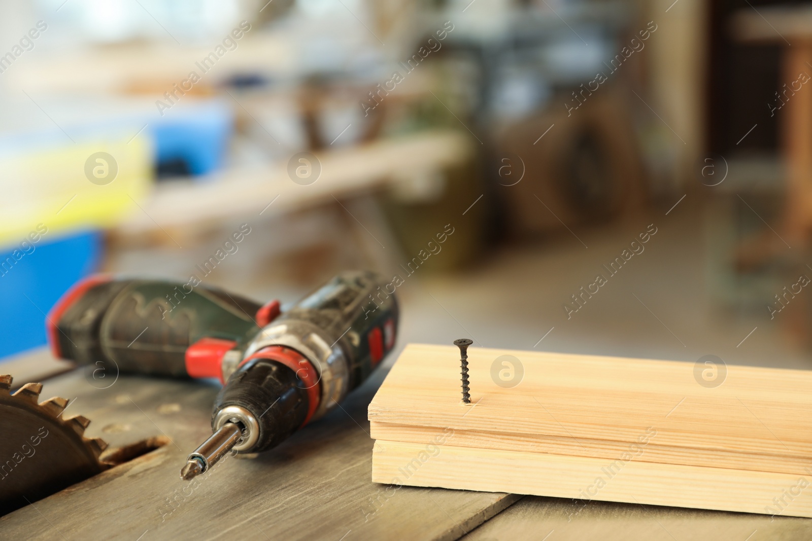 Photo of Carpenter's working place with electric screwdriver and timber strip on table indoors