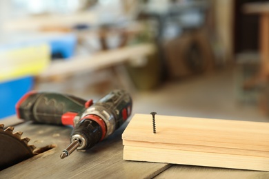 Photo of Carpenter's working place with electric screwdriver and timber strip on table indoors