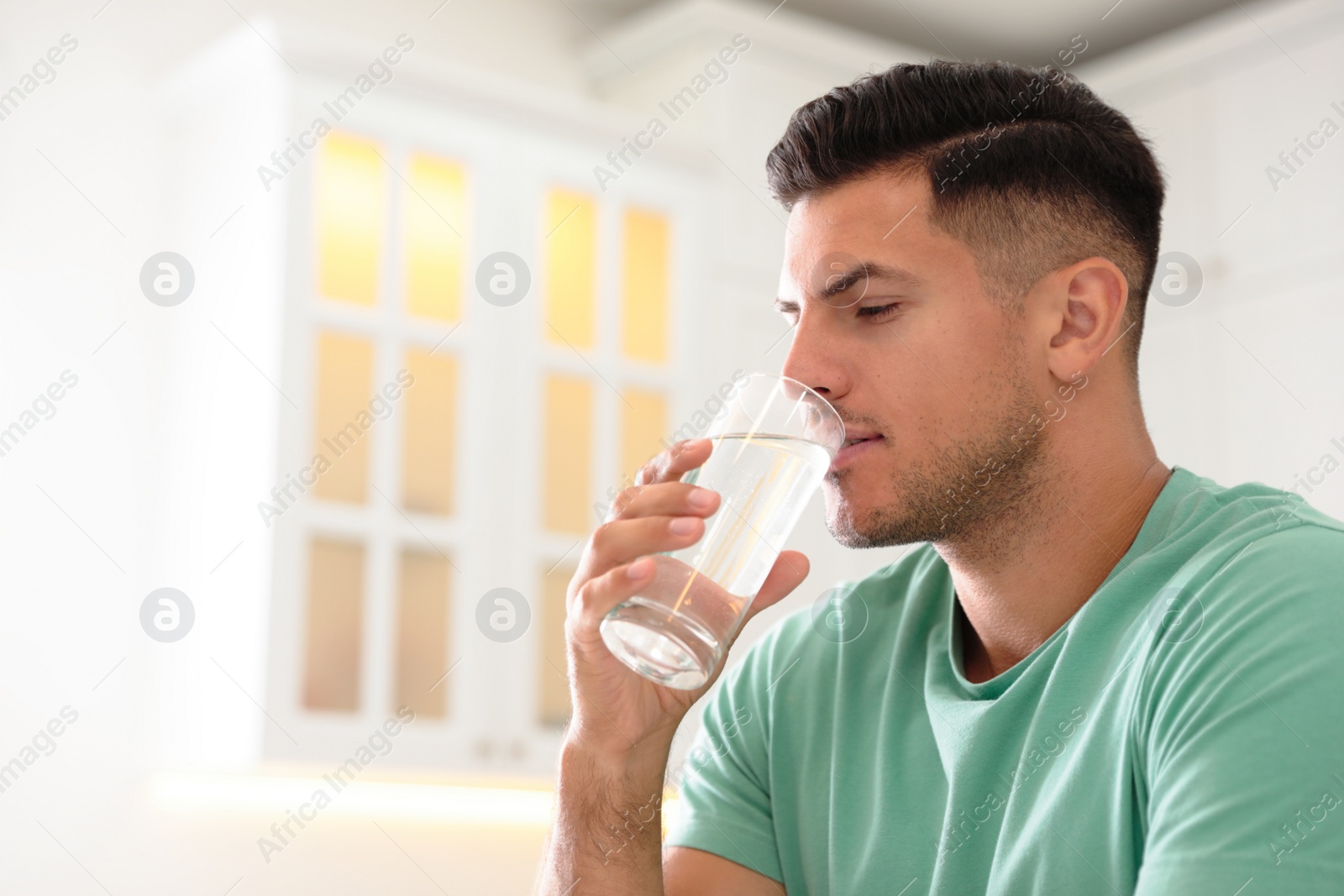 Photo of Man drinking pure water from glass in kitchen. Space for text