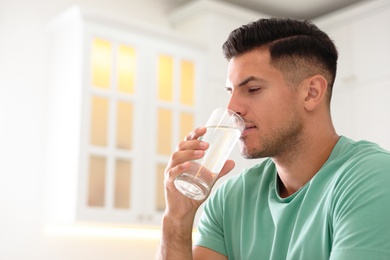 Man drinking pure water from glass in kitchen. Space for text