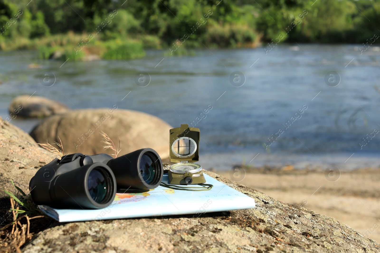 Photo of Binoculars, compass and map on stone near river, space for text. Camping equipment