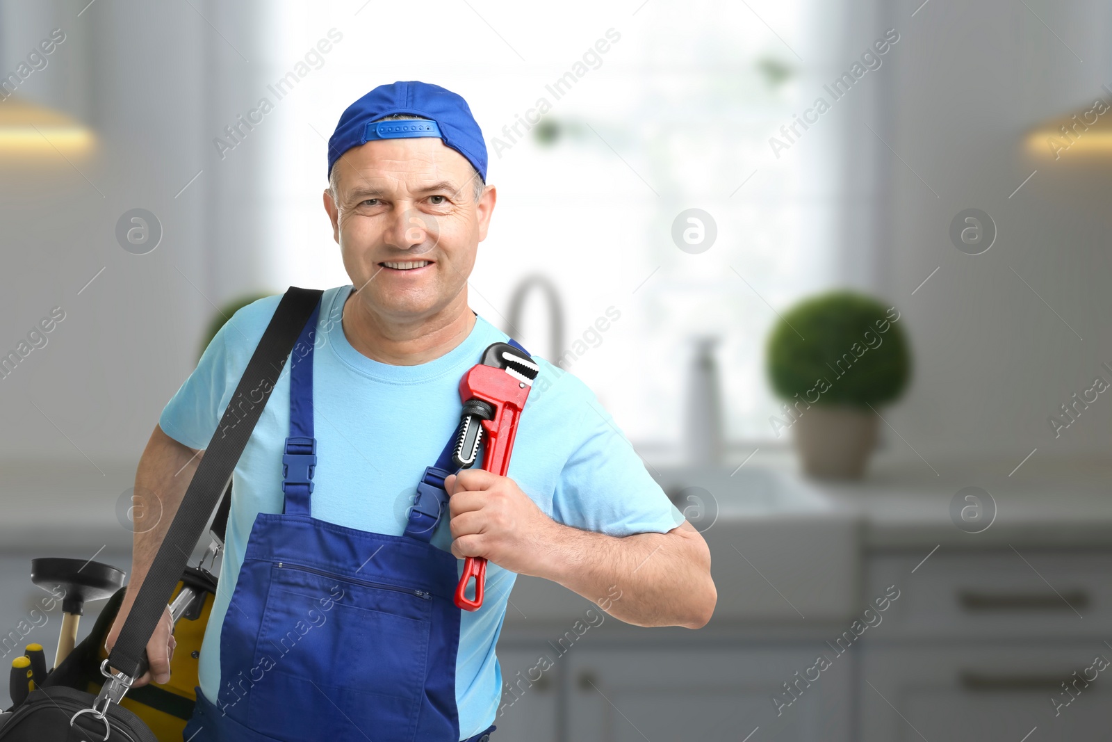 Image of Mature plumber with pipe wrench and tool bag in kitchen, space for text