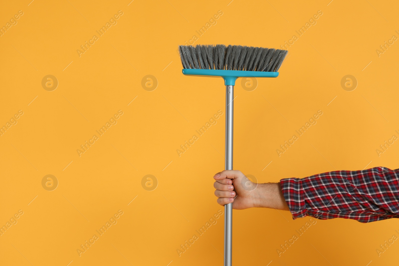 Photo of Young man with broom on orange background, closeup. Space for text