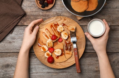 Photo of Woman eating delicious pancakes with strawberry, banana and syrup at table