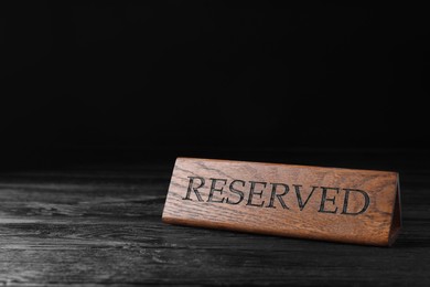 Elegant wooden sign RESERVED on black table, space for text