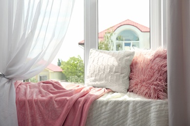 Photo of Soft pillows and plaids on sunlit window sill in room. Cozy place to relax