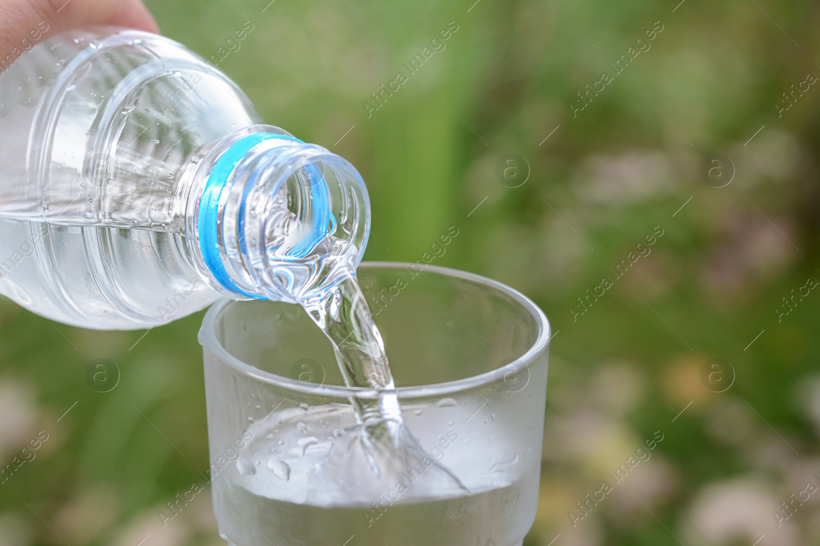 Photo of Woman pouring water from bottle into glass outdoors, closeup