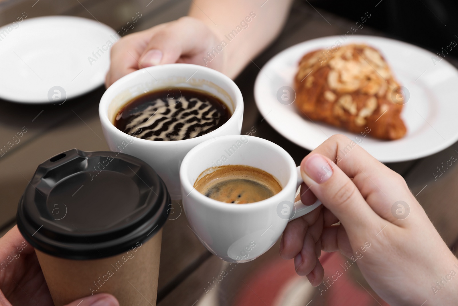 Photo of Friends drinking coffee at wooden table in outdoor cafe, closeup