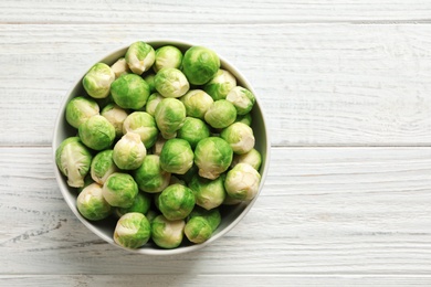 Photo of Bowl of fresh Brussels sprouts on wooden background, top view with space for text