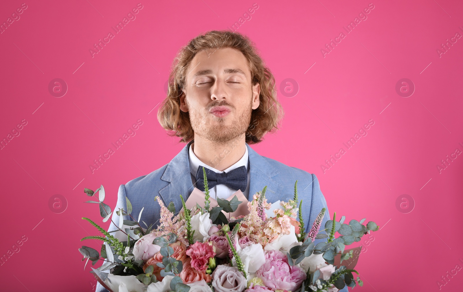 Photo of Young handsome man in stylish suit with beautiful flower bouquet on pink background