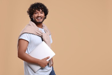 Smiling man with laptop on beige background, space for text