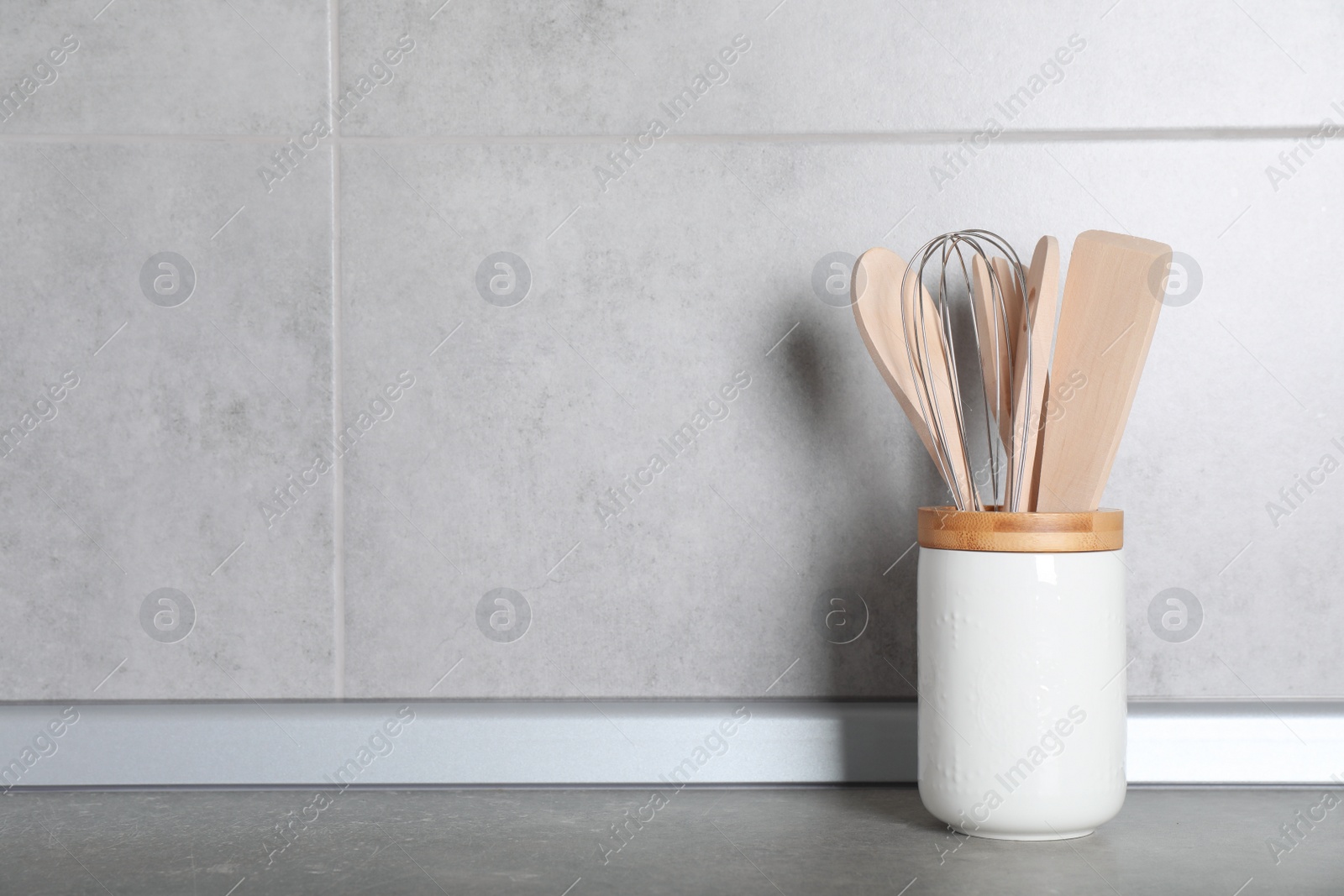 Photo of Holder with kitchen utensils on grey table. Space for text