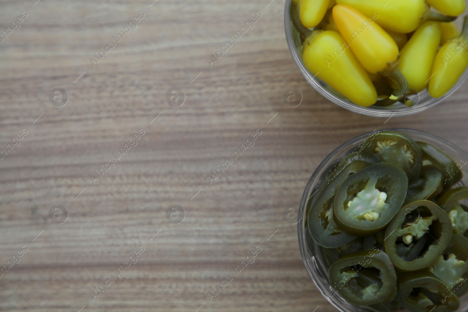 Photo of Glass bowls of pickled green and yellow jalapeno peppers on wooden table, flat lay. Space for text