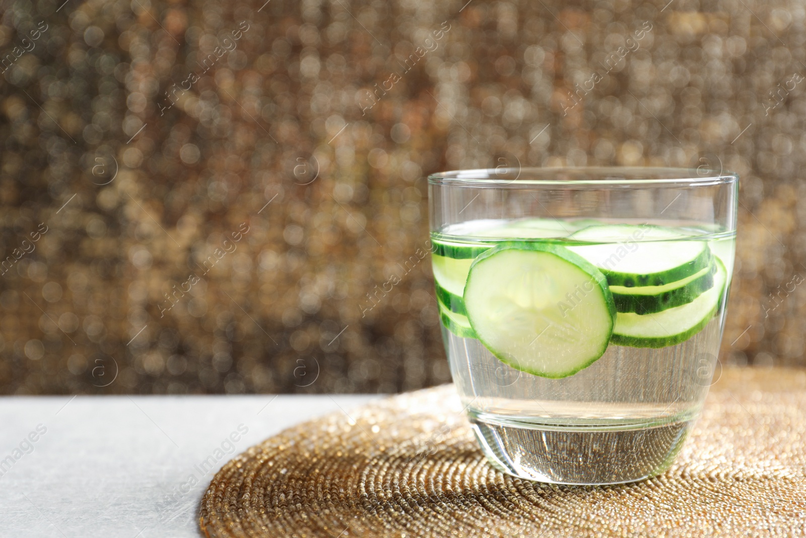 Photo of Glass of fresh cucumber water on golden mat. Space for text