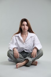 Beautiful young woman sitting on grey background