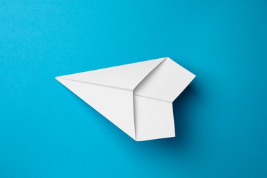 Photo of Handmade white paper plane on light blue background, top view