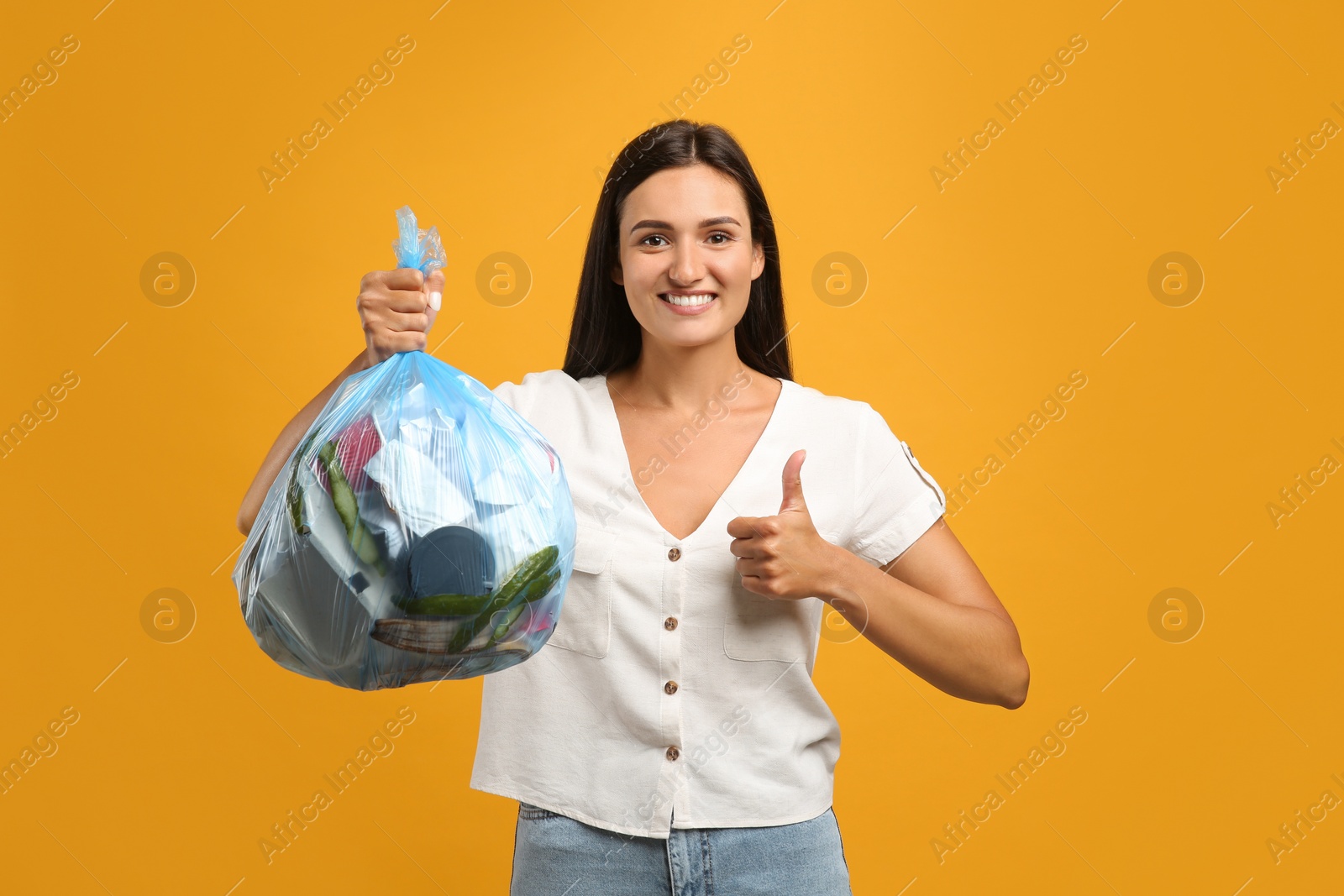 Photo of Woman holding full garbage bag on yellow background