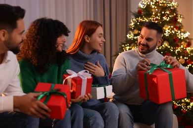Photo of Christmas celebration in circle of friends. Happy man opening gift at home