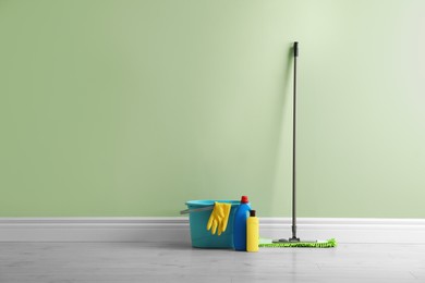 Mop and cleaning supplies on floor near green wall indoors, space for text