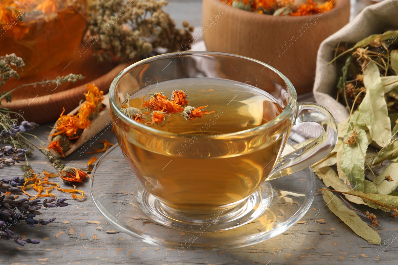 Photo of Freshly brewed tea and dried herbs on grey wooden table, closeup