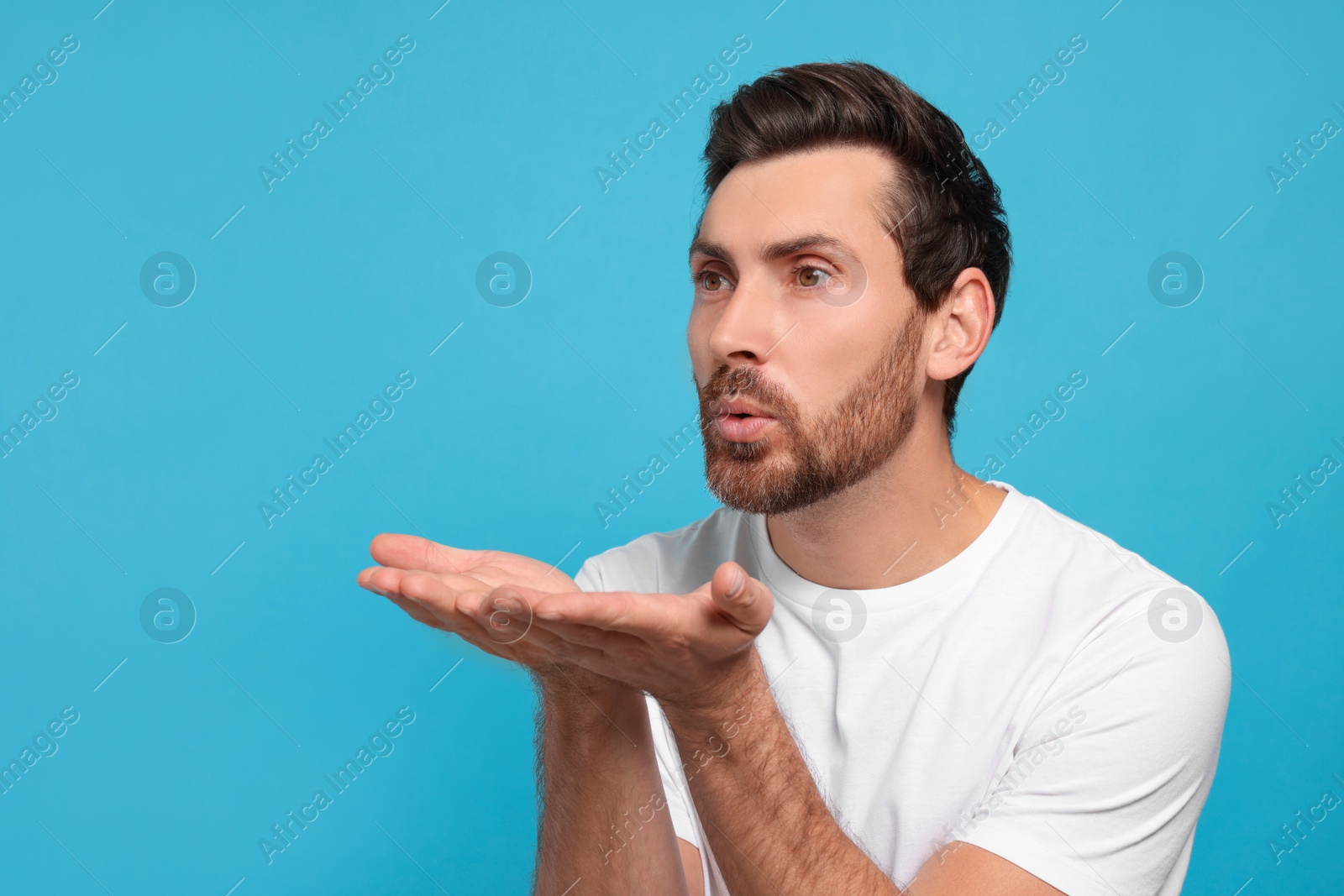 Photo of Handsome man blowing kiss on light blue background. Space for text