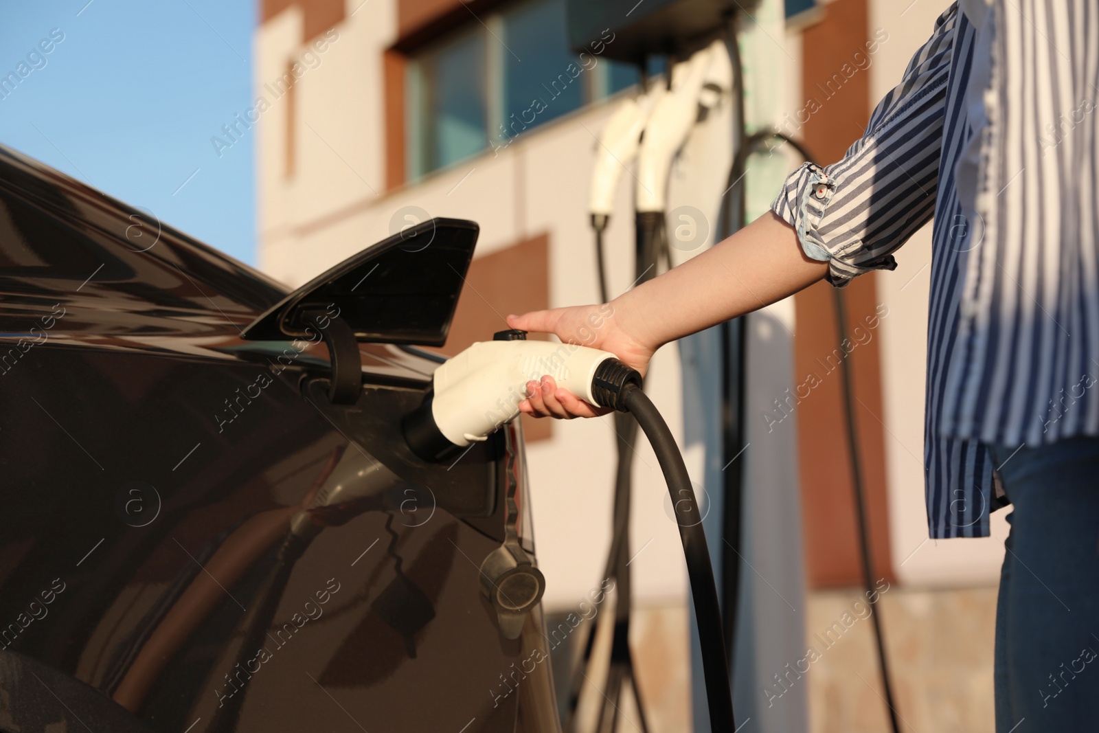 Photo of Woman inserting plug into electric car socket at charging station, closeup