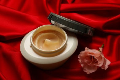 Photo of Open jar of hair care cosmetic product and beautiful flower on red fabric