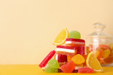 Photo of Pile of delicious bright jelly candies on yellow table. Space for text