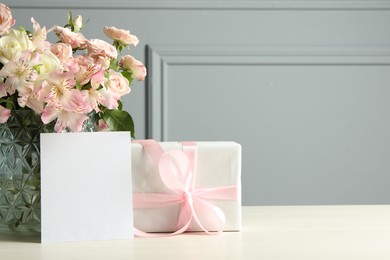 Happy Mother's Day. Gift box, blank card and bouquet of beautiful flowers in vase on white table near grey wall. Space for text