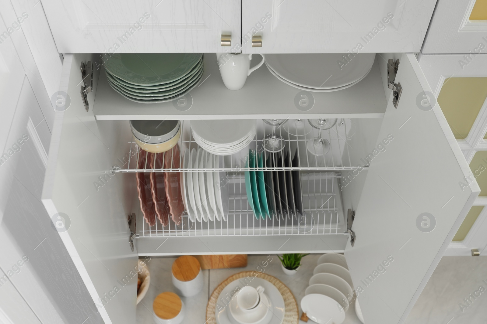 Photo of Clean plates, bowls and glasses on shelves in cabinet indoors