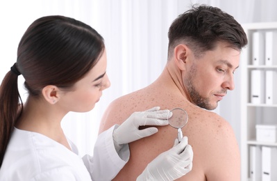 Dermatologist examining patient with magnifying glass in clinic