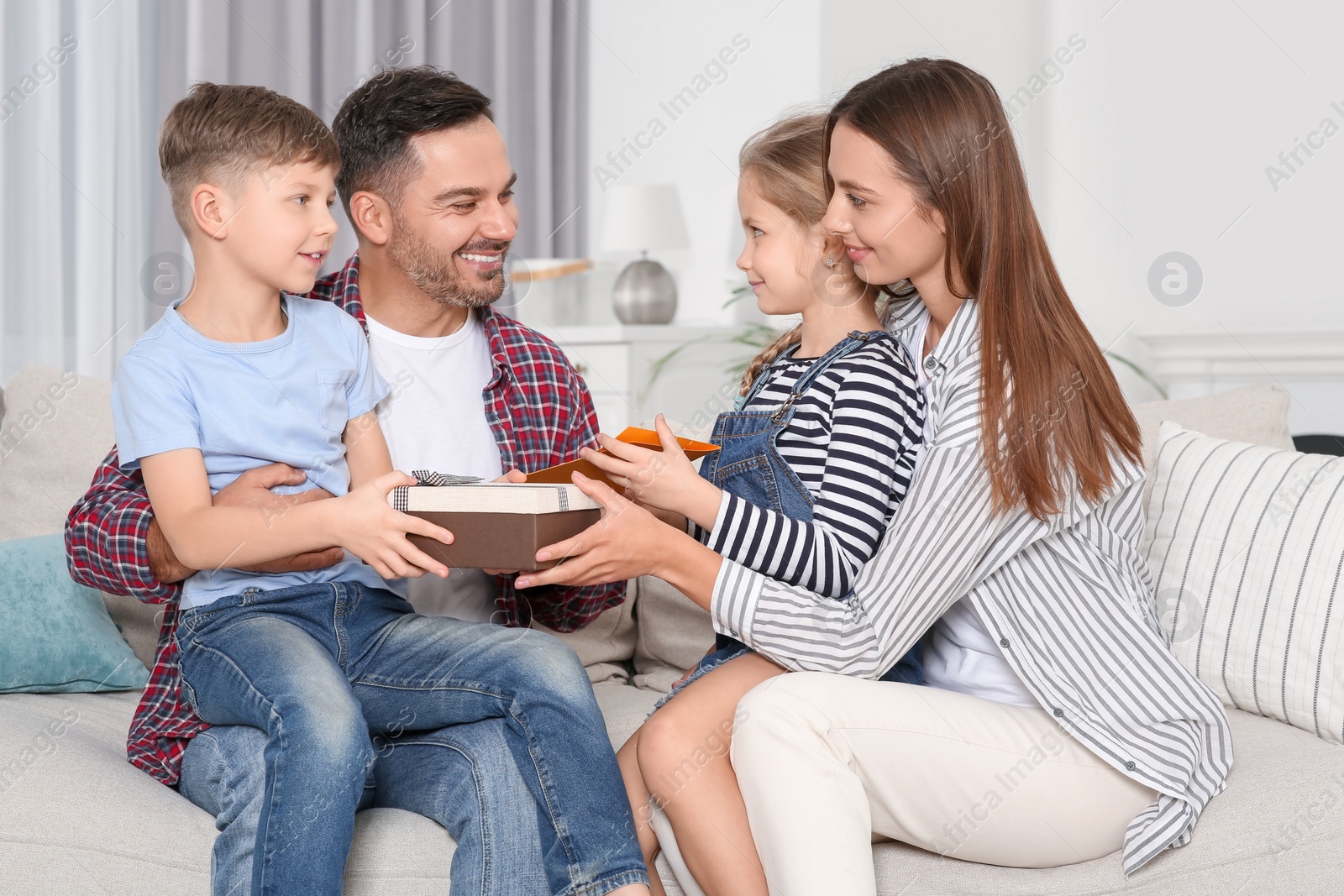 Photo of Happy family presenting each other with gifts on sofa at home