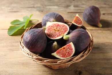 Photo of Wicker bowl with fresh ripe figs and green leaf on wooden table, closeup