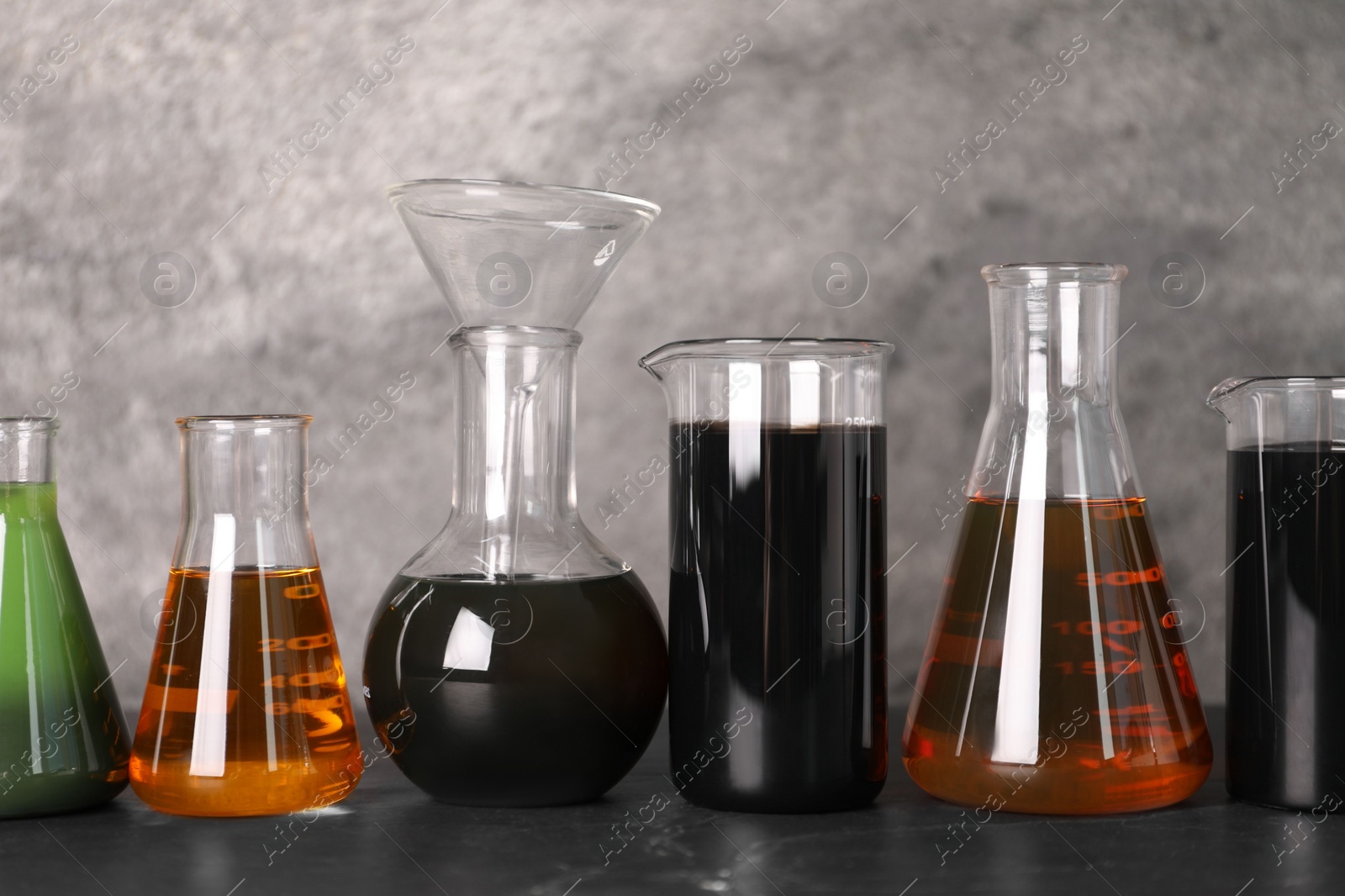 Photo of Beakers and flasks with different types of oil on grey textured table