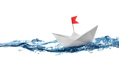 Image of Handmade paper boat floating on clear water against white background 