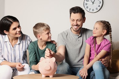 Photo of Happy family putting coin into piggy bank at home