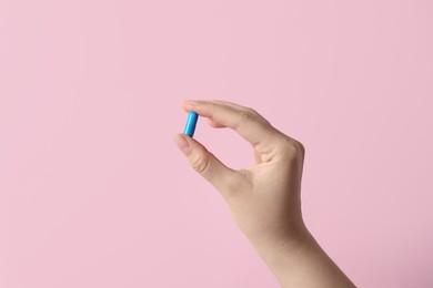 Woman holding pill on pink background, closeup