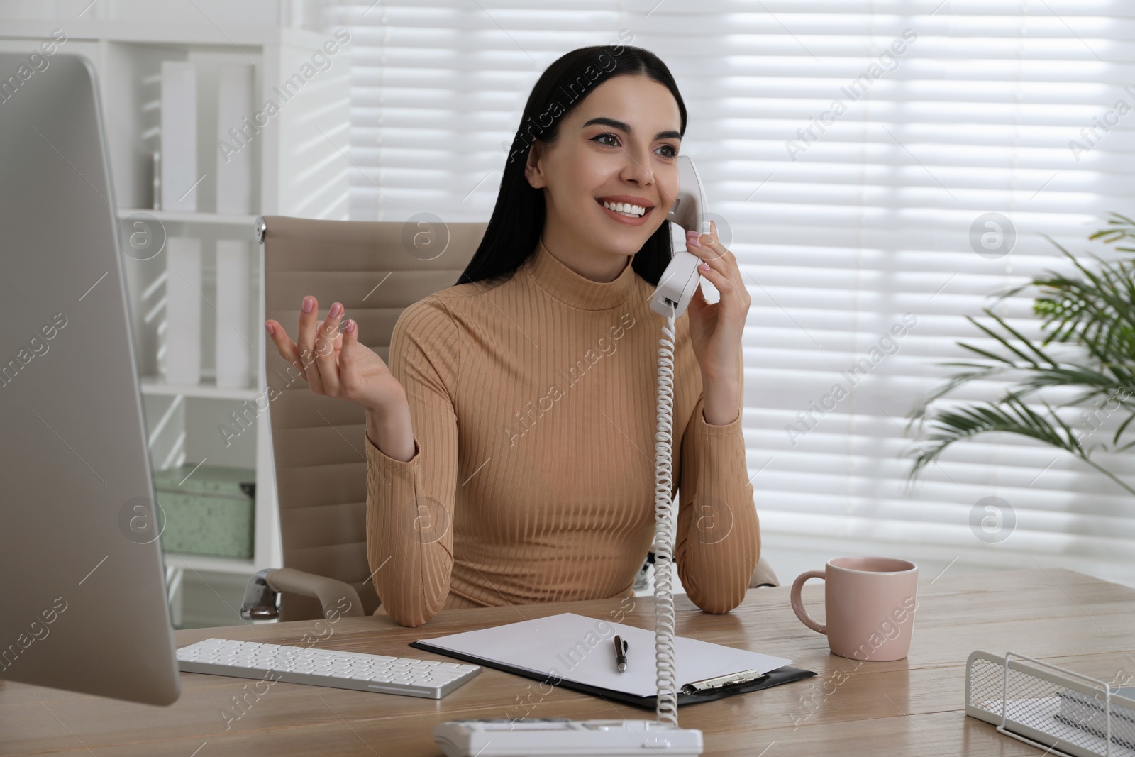 Photo of Secretary talking on phone at wooden table in office