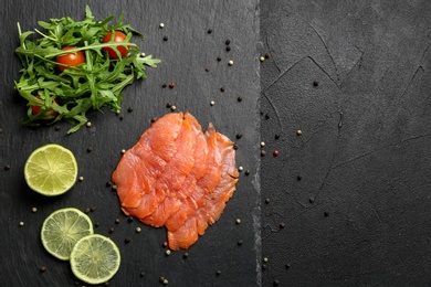 Photo of Fresh sliced salmon fillet with arugula and lemon on slate plate, top view