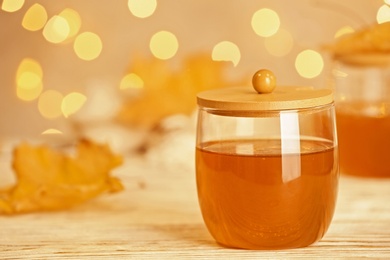 Photo of Glass jar with sweet honey on table against  blurred lights. Space for text