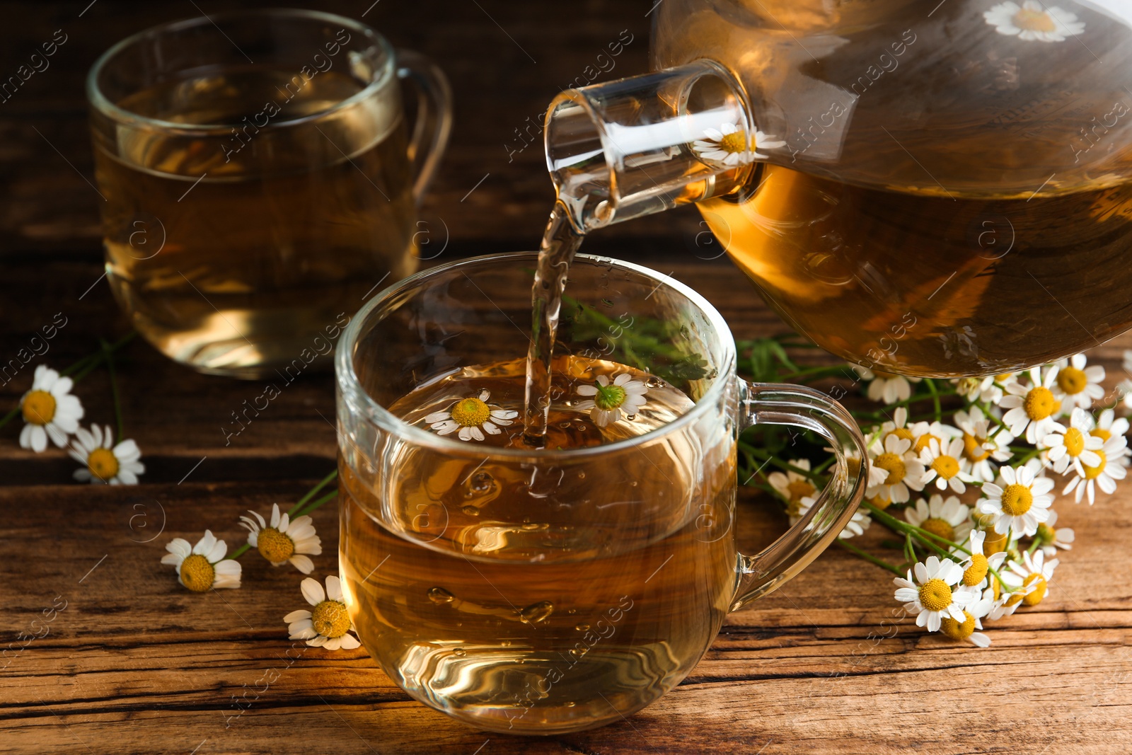 Photo of Pouring tasty chamomile tea into glass cup on wooden table