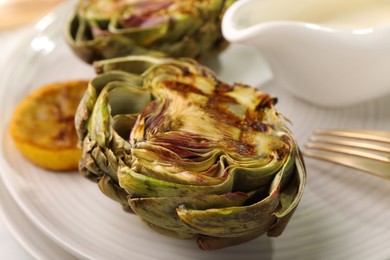 Photo of Tasty grilled artichokes on plate, closeup view