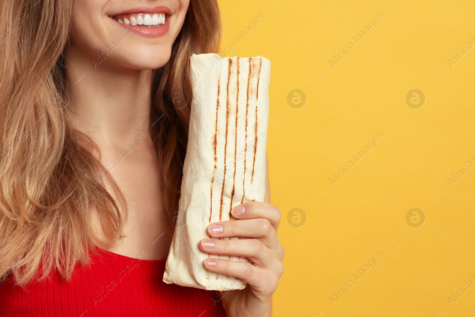 Photo of Young woman with delicious shawarma on yellow background, closeup. Space for text