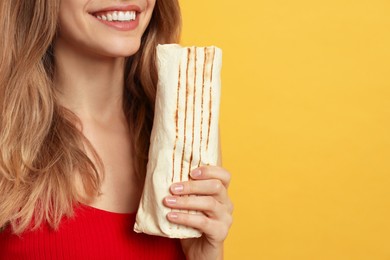 Photo of Young woman with delicious shawarma on yellow background, closeup. Space for text