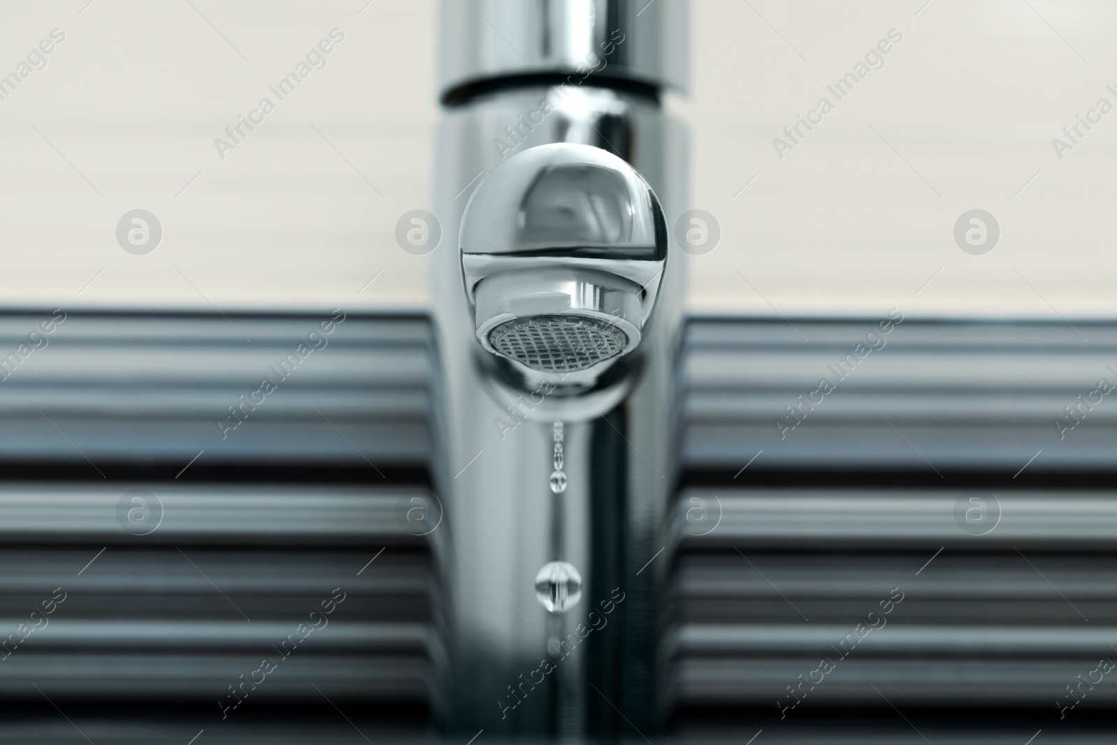 Photo of Water drops falling down from tap on blurred background, closeup