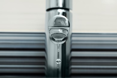 Photo of Water drops falling down from tap on blurred background, closeup