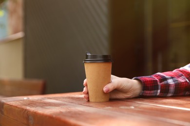 Man with takeaway coffee cup at wooden table outdoors, closeup. Space for text