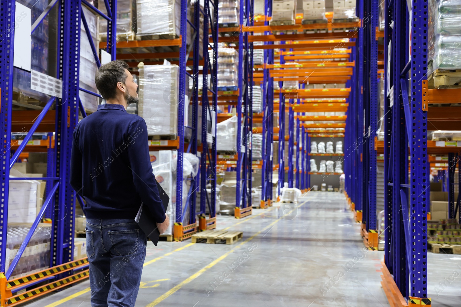 Photo of Manager holding clipboard in warehouse with lots of products, back view. Space for text