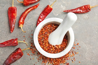 Photo of Mortar with crushed chili pepper and pods on grey background