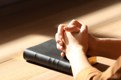Photo of Religious woman praying over Bible indoors, closeup